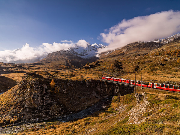 Unterwegs mit dem Bernina Express durch die herbstlich gefärbte hochalpine Landschaft auf dem Berninapass. Im Vordergrund die Brücke über die Ova da B
