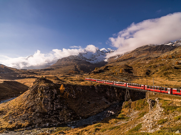 Unterwegs mit dem Bernina Express durch die herbstlich gefärbte hochalpine Landschaft auf dem Berninapass. Im Vordergrund die Brücke über die Ova da B