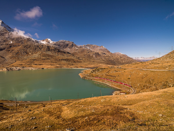 Der Bernina Express der Rhätischen Bahn unterwegs entlang des Lago Bianco auf dem Berninapass. Im Hintergrund die Crest d'Arlas, Piz Trovat und Sass Q