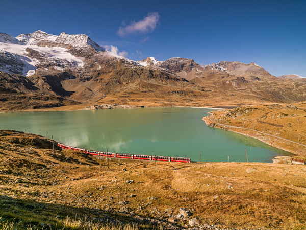 Der Bernina Express der Rhätischen Bahn unterwegs entlang des Lago Bianco auf dem Berninapass. Im Hintergrund Piz Caral, Piz Cambrena und Piz d'Arlas.