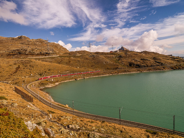Der Bernina Express der Rhätischen Bahn unterwegs entlang des Lago Bianco auf dem Berninapass. Im Hintergrund der Piz Campasc.