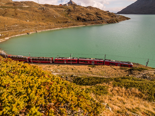 Der Bernina Express der Rhätischen Bahn unterwegs entlang des Lago Bianco auf dem Berninapass. Im Hintergrund der Piz Campasc.