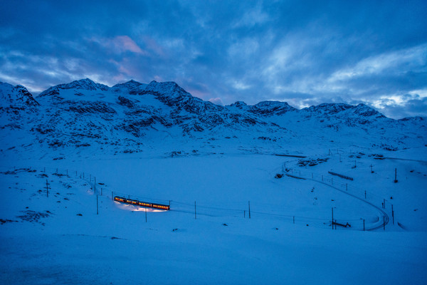 Die Rhätische Bahn auf dem Berninapass im Oberengadin. Im Hintergrund der zugeschneite Lago Bianco sowie die Berge Piz Caral, Piz Cambrena und Piz d'A