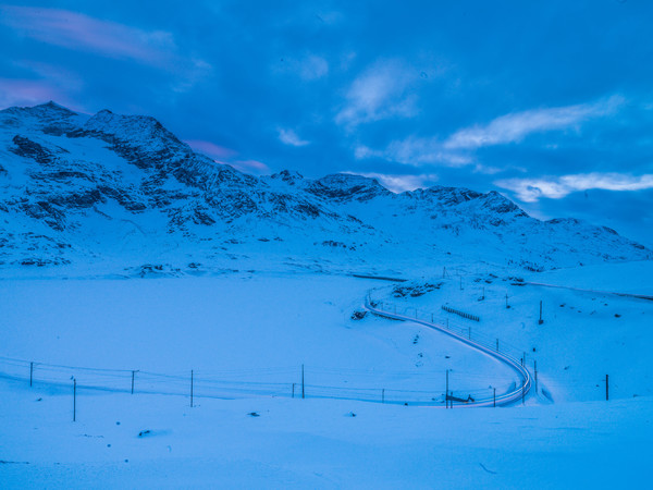 Die Rhätische Bahn auf dem Berninapass im Oberengadin. Im Hintergrund der zugeschneite Lago Bianco sowie die Berge Piz Caral, Piz Cambrena und Piz d'A