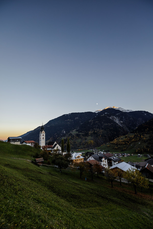 Blick auf das Bergdorf Sumvitg mit seinem markanten Kirchturm in der Abendstimmung im Bündner Oberland, Graubünden, Schweiz.